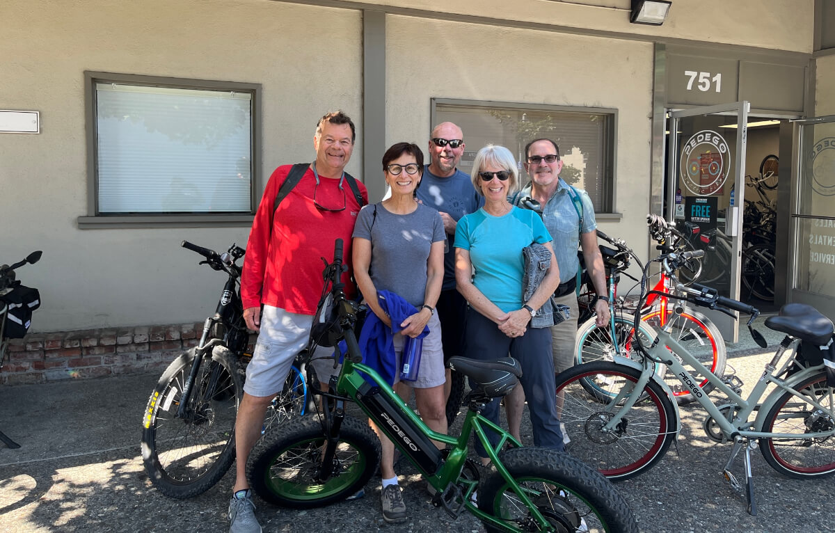 A group of five people standing and smiling with their e-bikes