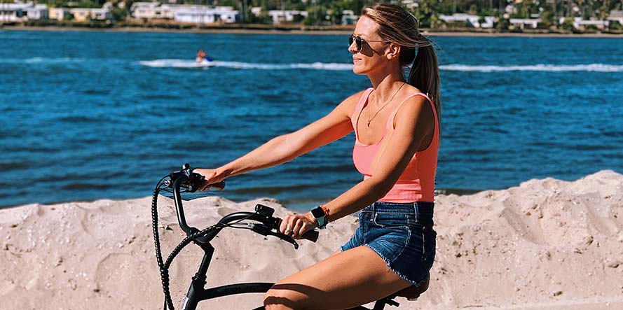 A blue pedego e-bike propped on a cliff with the pacific ocean in the background