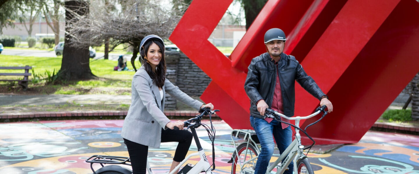 A woman and man smiling, posing for a picture on their e-bikes.